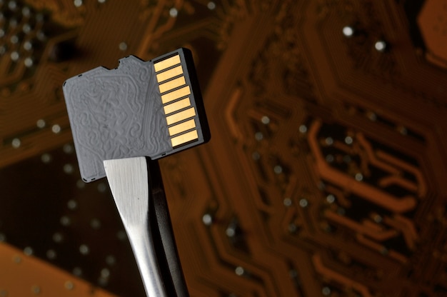 Close-up van een Micro SD-geheugenkaart tegen een microschakeling, vastgeklemd met een pincet.