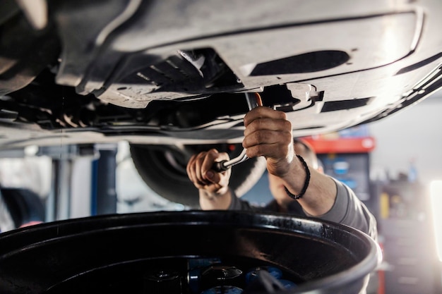 Close-up van een monteur die een versprongen sleutel op een auto gebruikt terwijl hij eronder staat in de winkel van monteur