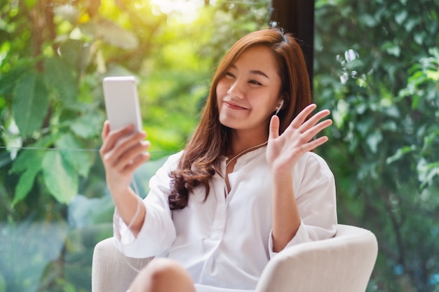 Close-up van een mooie Aziatische vrouw die handen golft terwijl thuis het gebruiken van mobiele telefoon voor videogesprek