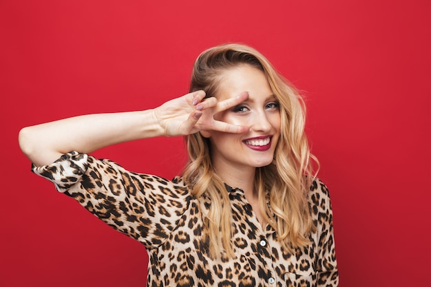 Close-up van een mooie jonge blonde vrouw die make-up draagt ?? camera kijken, poseren geïsoleerd dan rood