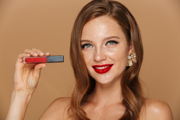 Close-up van een mooie jonge vrouw, gekleed in make-up en sieraden accessoires poseren geïsoleerd over beige muur, rode lipgloss tonen