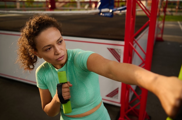 Close-up van een mooie vastberaden sportieve vrouw in beweging, trainen op het sportveld, boksen met kleine halters, een cardiotraining uitvoeren