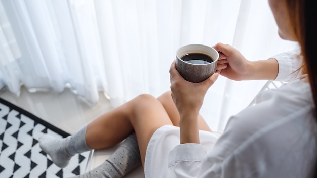 Close-up van een mooie vrouw die hete koffie in slaapkamer thuis in de ochtend drinken