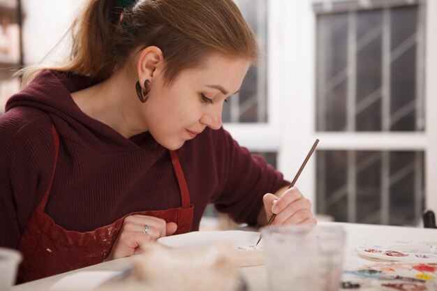 Close-up van een mooie vrouw die lacht en een keramische plaat schildert op aardewerkles