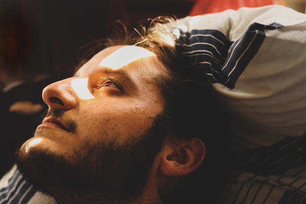 Close-up van een nadenkende jonge man die wegkijkt terwijl hij op bed ligt