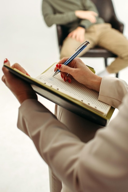 Close-up van een notitieboek met een pen in de handen van een psycholoog die notities maakt tijdens een psychotherapiesessie met een man Psychologie psychotherapie verticaal kader