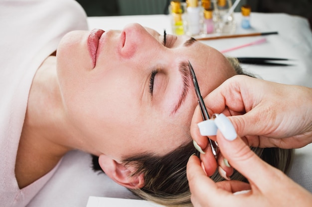 Close up van een onherkenbare make-up artiest handen doen wenkbrauw lamineren procedure aan mooie volwassen vrouw.