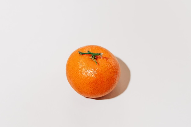 Close-up van een oranje mandarijn met een tak verlicht door een hard licht liggend op een witte geïsoleerde achtergrond afbeelding voor uw ontwerp