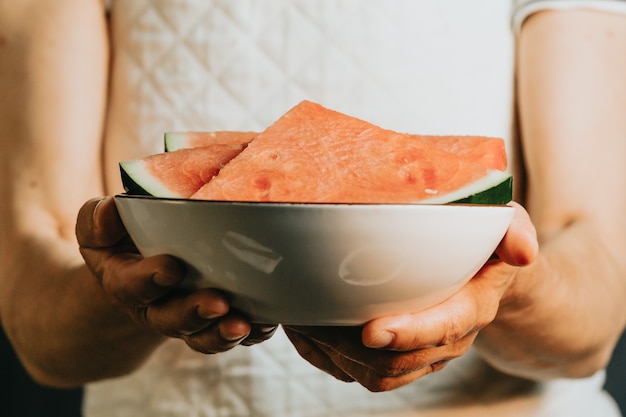 Close-up van een oude serveerster biedt en houdt een watermeloen in een gerecht, fruit, gezond leven, goed eten, mediterrane concepten, kopieerruimte, verticaal beeld