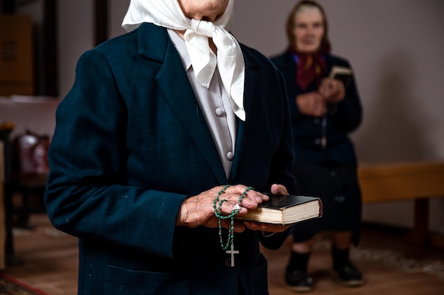 Close-up van een oude vrouw die een Bijbel en een rozenkrans in haar handen houdt in een katholieke kerk en bidt