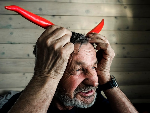 Foto close-up van een oudere man die hoorns maakt met rode chili pepers