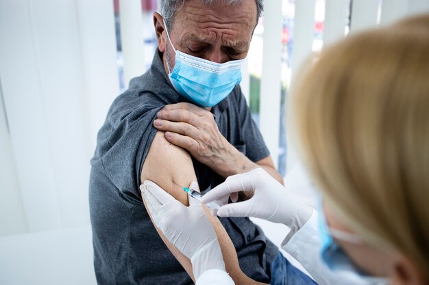 Close-up van een oudere man die tijdens een coronavirus-pandemie in zijn arm wordt gevaccineerd.