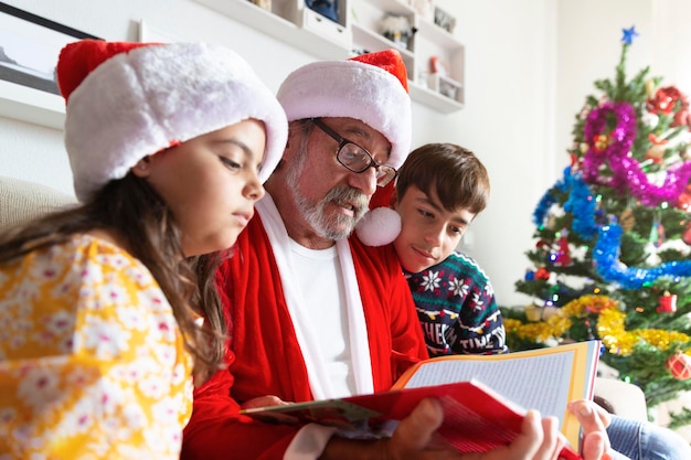 Close-up van een oudere man verkleed als kerstman die thuis een verhaal voorleest aan twee kinderen