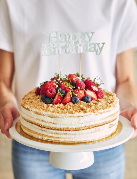 Close-up van een persoon die de fruitige cake vasthoudt met een "Happy Birthday"-topper