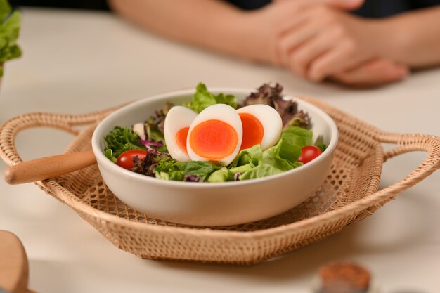 Close-up van een plaat van salade met gekookte eieren, sla en tomaat op rieten dienblad in restaurant