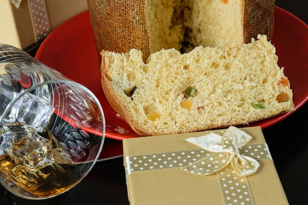 Close-up van een plakje panettone naast een omgedraaid whiskyglas en een geschenkdoos.