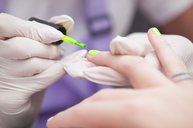 Close-up van een professionele manicure die neonnagelgel gebruikt op de nagels van de klant