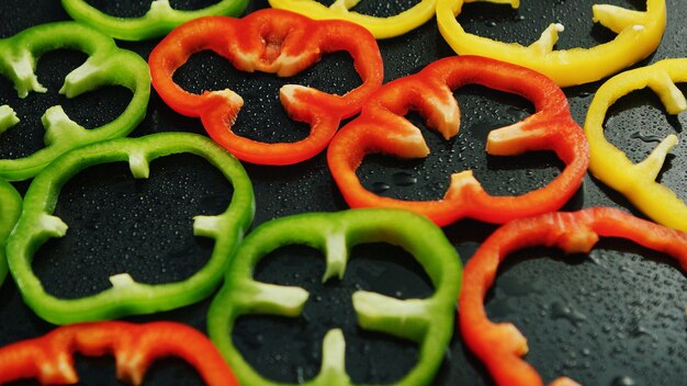 Foto close-up van een samengestelde laag veelkleurige ringen van gesneden paprika's op nat oppervlak