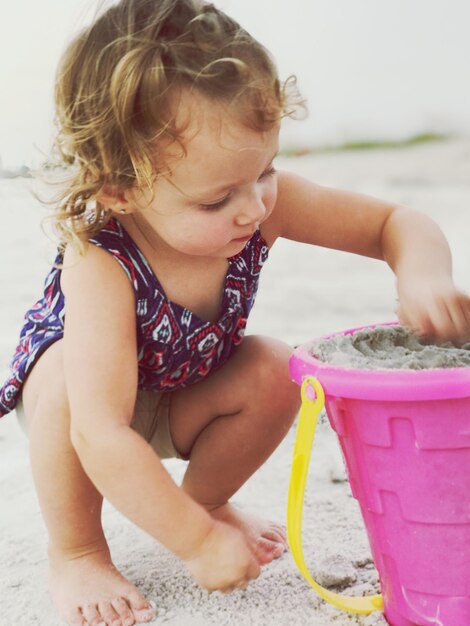 Close-up van een schattig baby meisje dat met zand speelt terwijl het op het strand kruipt