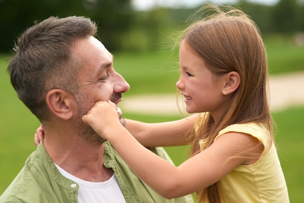 Close-up van een schattig klein meisje dat plezier heeft met haar liefhebbende vader die zijn gezicht aanraakt terwijl hij is