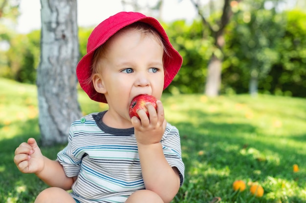 Close-up van een schattige jongen die een appel eet en op het gras zit.
