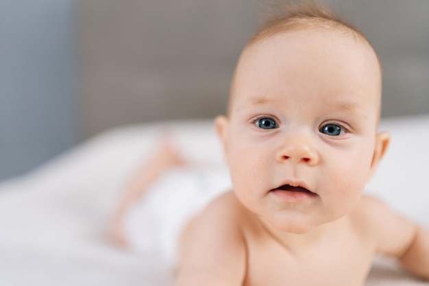 Close-up van een schattige pasgeboren baby die in bed ligt en probeert te kruipen en thuis met zijn hand zwaait.