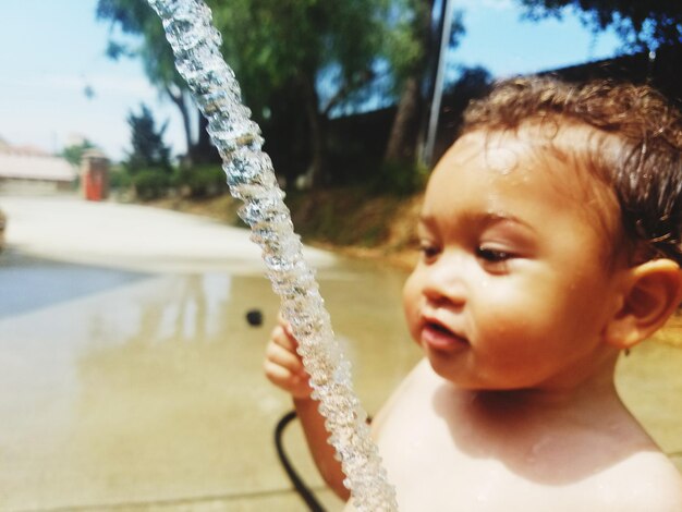 Foto close-up van een schattige shirtloze baby jongen die water spat op het strand