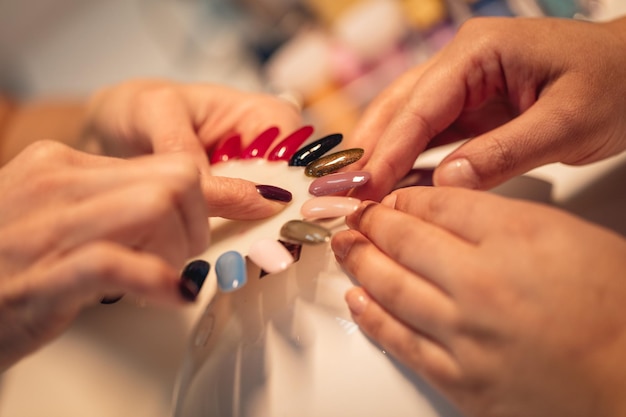 Close-up van een schoonheidsspecialiste en vrouwelijke klanten die monsters vasthouden en kleuren nagels kiezen in de schoonheidssalon.