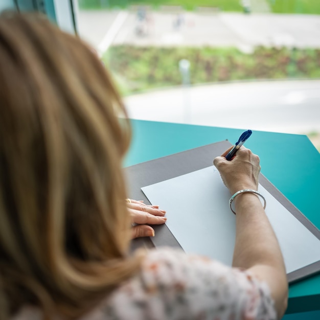 Close-up van een schrijvende vrouw van achter en naast een enorm raam dat uitkijkt op de buitenkant