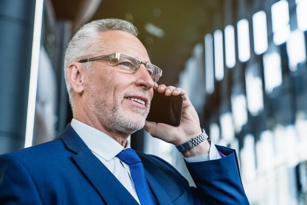 Close-up van een senior blanke zakenman die in een kantoorcafé staat en aan de telefoon praat