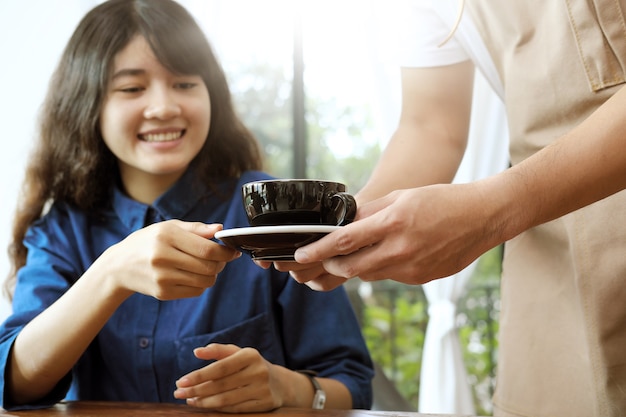 Close-up van een serveerster serveren een kopje koffie aan jonge mooie klant.