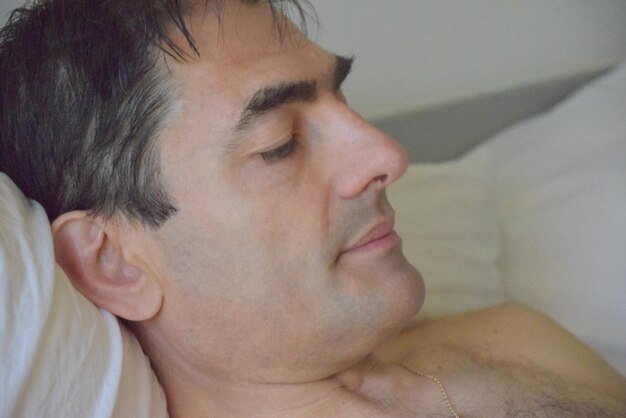 Foto close-up van een shirtloze man die thuis op bed ontspant.