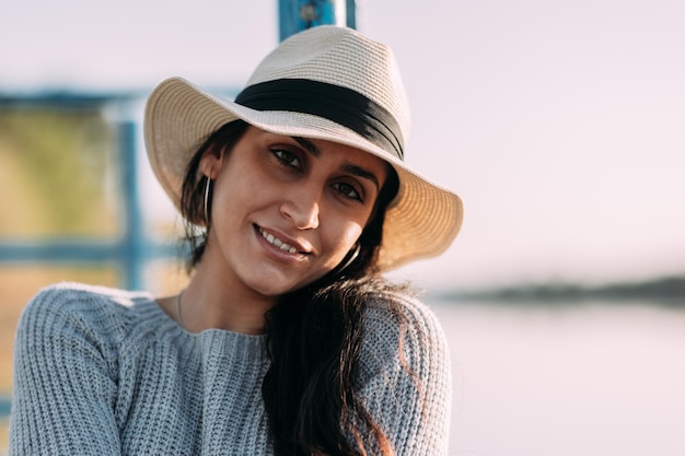 Close-up van een Spaanse jonge vrouw die lacht met een hoed aan de rand van een dok naast een meer