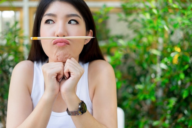 Close-up van een speelse jonge vrouw die een potlood op haar lippen houdt