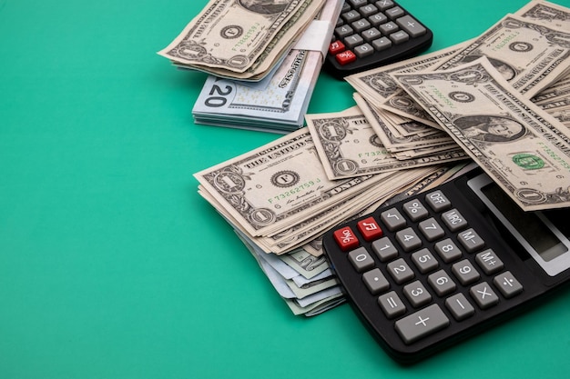 Close-up van een stapel dollarbiljetten, omgeven door zwarte rekenmachines, op een groene tafel.