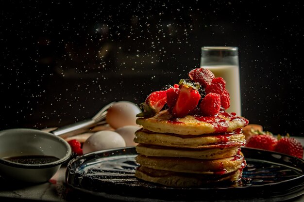 Close-up van een stapel smakelijke pannenkoeken gegarneerd met aardbeien en ingrediënten op de achtergrond