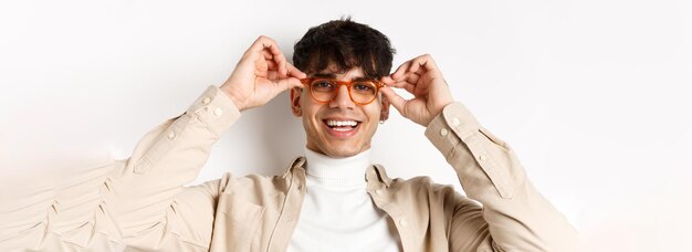 Close-up van een stijlvolle hipster-man die een bril probeert in de opticienwinkel, zet een bril op en glimlacht staand