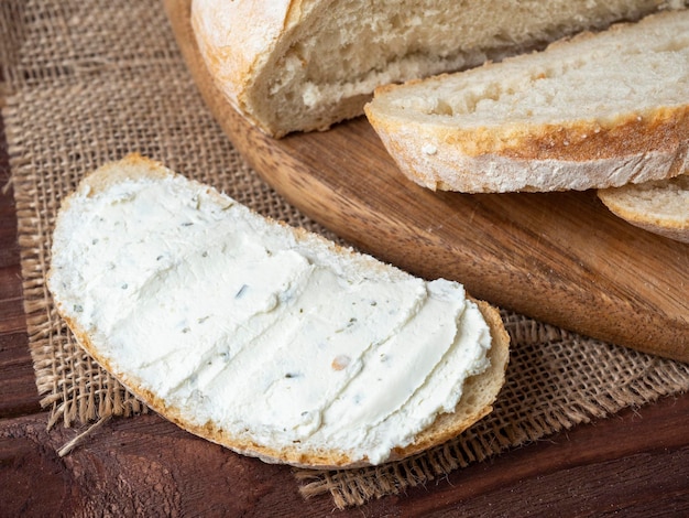 Close-up van een stuk brood besmeurd met kwark naast vers brood linnen servet houten bruine achtergrond bovenaanzicht plat lag