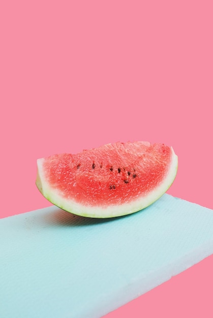 Close-up van een stukje watermeloen op een snijplank tegen een roze achtergrond