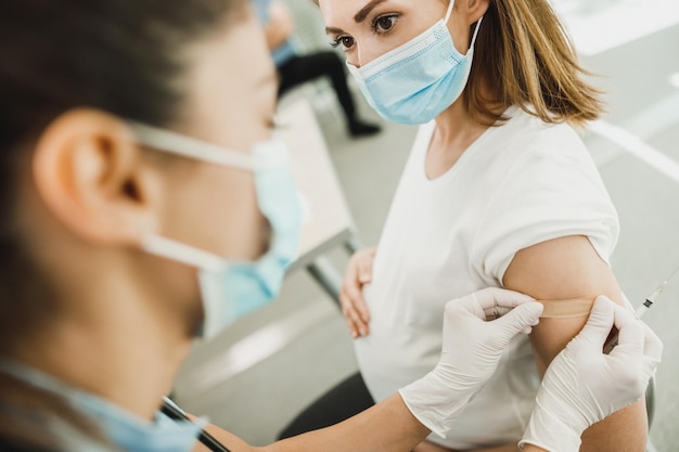 Close-up van een verpleegster die een pleister aanbrengt op een jonge zwangere vrouw na ontvangst van een vaccin als gevolg van een coronavirusepidemie.