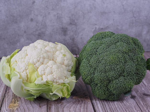 Foto close-up van een verse en rauwe broccoli en bloemkool gezond en vegetarisch eten op houten tafel en grijze achtergrond