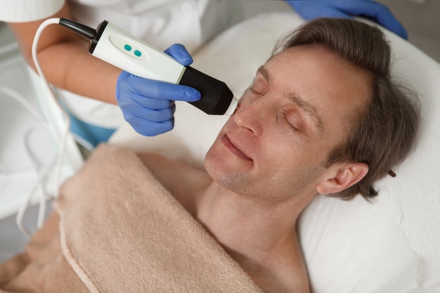 Close up van een volwassen man ontspannen in schoonheidskliniek tijdens cosmetische hardware behandeling