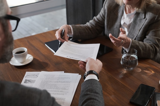 Close-up van een volwassen zakenman die een zakelijk contract geeft aan een zakenvrouw om het te ondertekenen tijdens een bijeenkomst in café