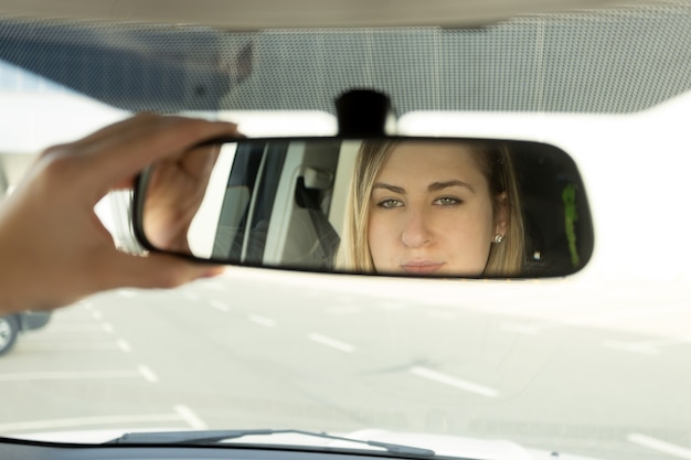 Foto close-up van een vrouw die de autospiegel aanpast en in de reflectie kijkt