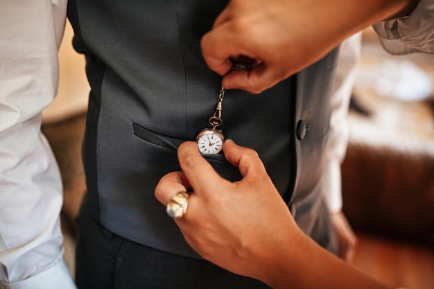 Close-up van een vrouw die de man helpt om zich klaar te maken op zijn trouwdag en zakhorloge in zijn vest te stoppen