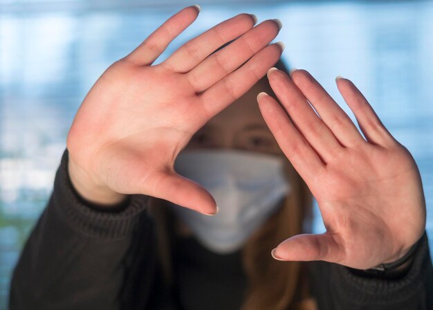 Foto close-up van een vrouw die een medisch masker draagt en stopt met gebaren met beide handen