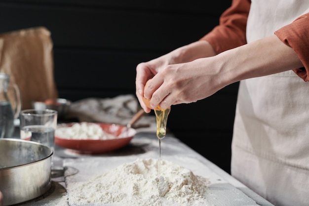 Close-up van een vrouw die egga toevoegt en een deeg maakt tijdens het bakken van de taart in de keuken