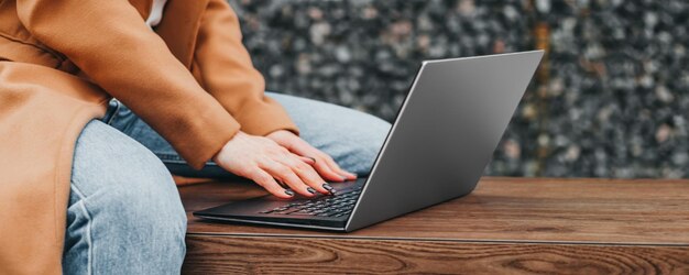 Close-up van een vrouw die haar handen typt in een laptop op straat tegen de achtergrond van een kantoorgebouw