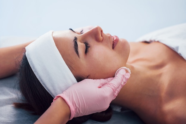 Close-up van een vrouw die in de spa-salon ligt en een gezichtsreinigingsprocedure heeft door schoonheidsspecialist in handschoenen.