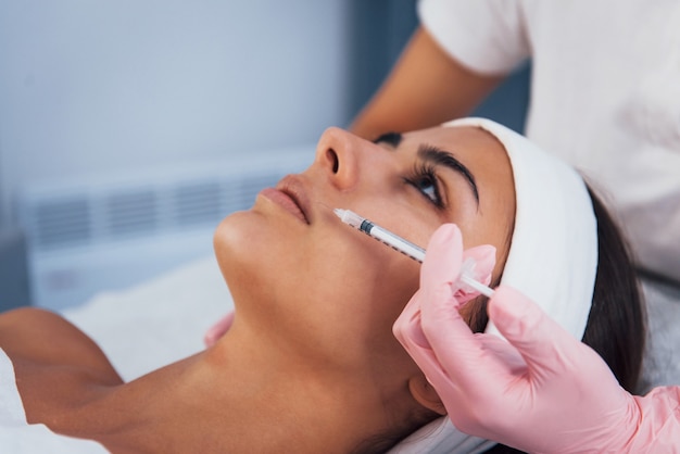 Close-up van een vrouw die in de spa-salon ligt en met de spuit in de huid van haar gezicht wordt geïnjecteerd.